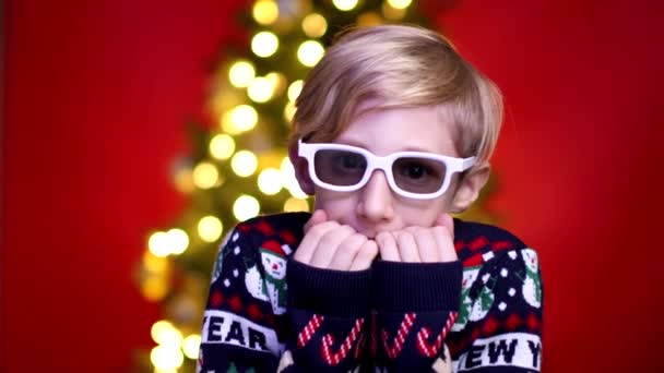 Een kind in een kersttrui op de achtergrond van een kerstboom — Stockvideo