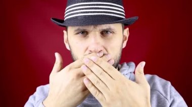 Sakallı ve siyah şapkalı bir adam elleriyle ağzını kapatıyor.