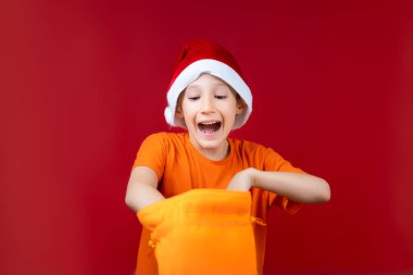 Noel Baba şapkalı bir çocuk sarı bir Noel hediyesi çantasıyla ortalığı karıştırıyor ve yüksek sesle gülüyor.