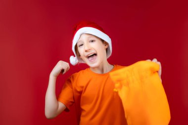 Noel Baba şapkalı neşeli bir çocuk elinde hediyelerle bir yılbaşı çantası tutuyor.