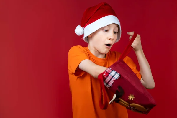 Мальчик Красном Фоне Шляпе Санта Клауса Держит Подарочный Пакет Руках — стоковое фото