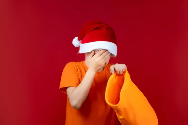 Kırmızı Arka Planda Noel Baba Şapkası Takan Bir Çocuk Elinde — Stok fotoğraf