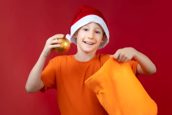 Wesoły Chłopiec Kapeluszu Mikołaja Torbą Świąteczną Wyciągnął Zabawkę Choinkę Piłkę — Zdjęcie stockowe