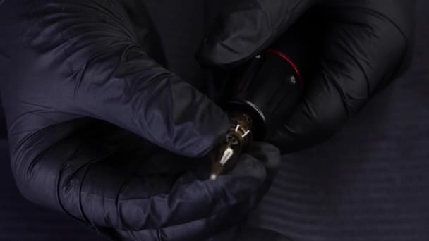 Ręce mistrza w czarnych rękawiczkach trzymają maszynę do tatuażu i próbują — Wideo stockowe