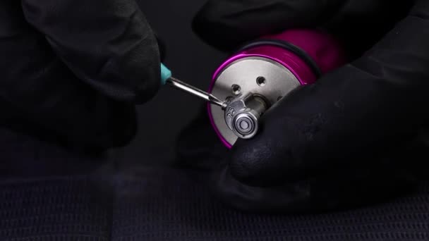 Ein Meister in schwarzen Handschuhen schraubt eine Schraube von einer Tätowiermaschine ab — Stockvideo