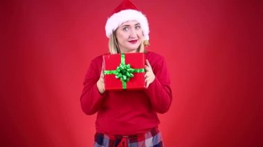 Kırmızı pijamalı güzel bir kadın ve Noel Baba şapkası bir hediyeyi sallıyor.