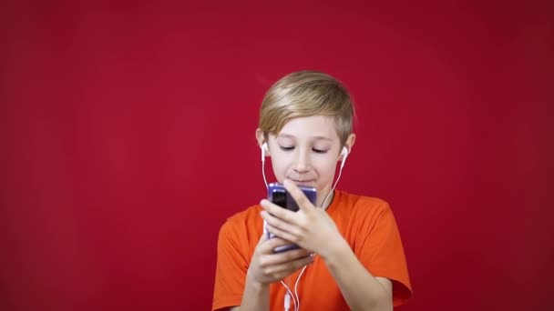 红色背景的男孩在他面前拿着电话，打开他最喜欢的轨道 — 图库视频影像