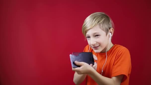 Pojke med hörlurar i öronen lyssnar på musik och skjuter från telefonen — Stockvideo