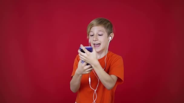 Menino, segurando um telefone na frente dele, ouvindo música através de fones de ouvido — Vídeo de Stock
