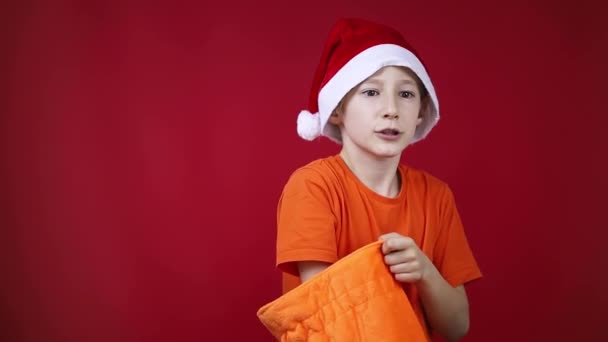 Un ragazzo in un cappello di Natale Babbo Natale è alla ricerca di regali in una borsa e non trova — Video Stock