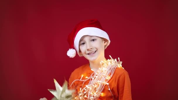 Jongen met een kerstmuts heeft een bloemenslinger om zijn nek die gloeit — Stockvideo