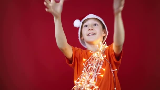 Een jongen in kerstkleren met een bloemenslinger om zijn nek vangt een nieuwjaar — Stockvideo