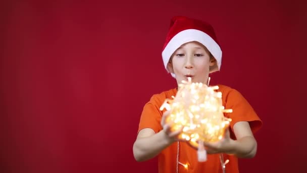 Jongen in een kerstman hoed draait een streng van Kerst slingers voor hem dat gloeien — Stockvideo
