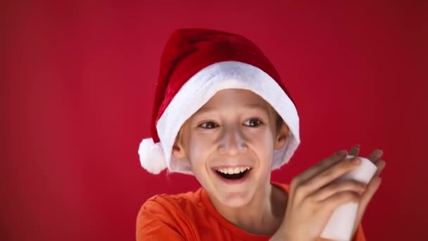 Un niño alegre en un sombrero de Santa es muy feliz cuando se frota las palmas con una esponja — Vídeos de Stock