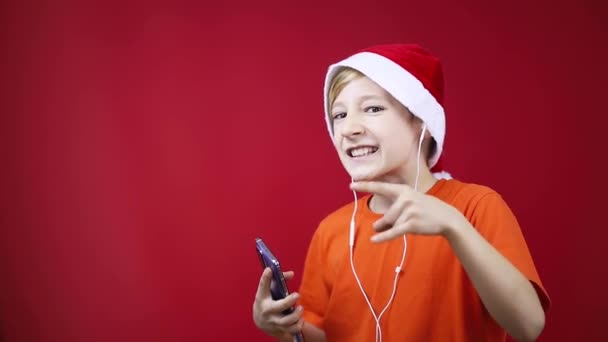 Chico en un sombrero de Navidad baila y canta a la música rock muestra gestos de heavy metal — Vídeos de Stock
