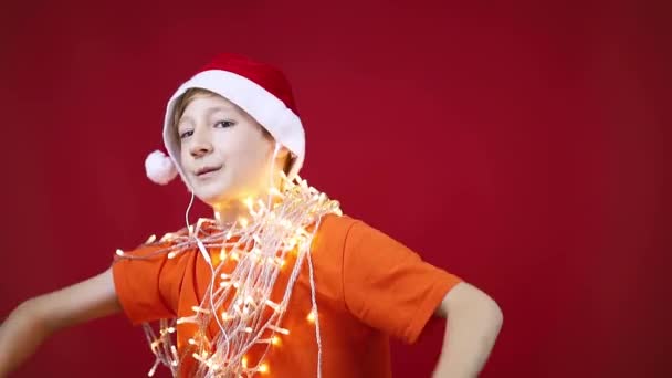 Αστείο αγόρι με Χριστουγεννιάτικα ρούχα με μια γιρλάντα γύρω από το λαιμό του να χορεύει — Αρχείο Βίντεο