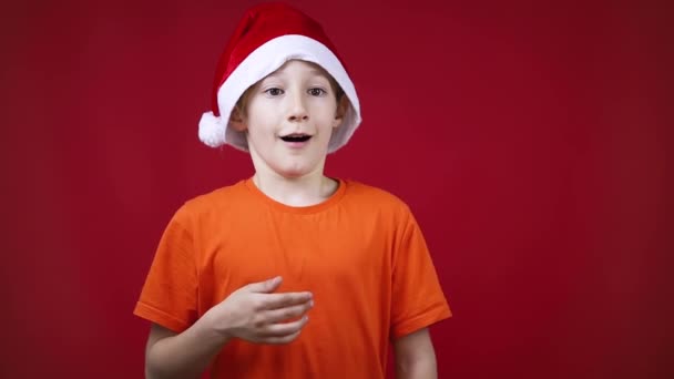 Un ragazzo sorpreso in un cappello rosso di Babbo Natale mette la mano in una borsa regalo — Video Stock
