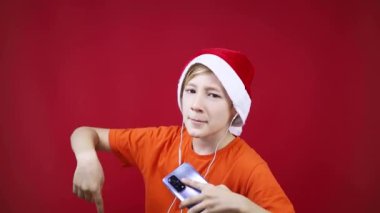 Kırmızı arkaplanda Noel şapkalı bir çocuk dans ediyor