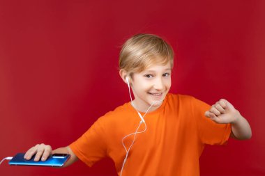 Kırmızı arka planda gülümseyen güzel bir çocuk elinde bir telefon tutuyor ve kulaklıkla müzik dinliyor.