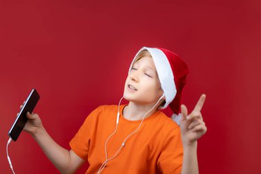 Noel Baba 'nın şapkalı çocuğu kulaklarında kulaklıklarla dans edip şarkı söylüyor.