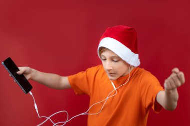 Sarı tişörtlü ve kırmızı şapkalı bir çocuk telefonu elinde tutuyor ve kulaklıkla müzik dinliyor.