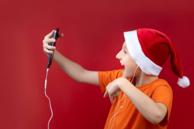 Noel Baba şapkalı bir çocuk telefonu önünde tutuyor ve neşeyle bağırıyor.