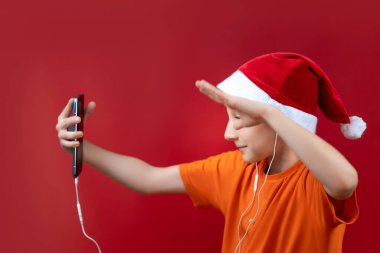 Noel Baba şapkalı bir çocuk telefonu önünde tutuyor ve neşeyle bağırıyor.