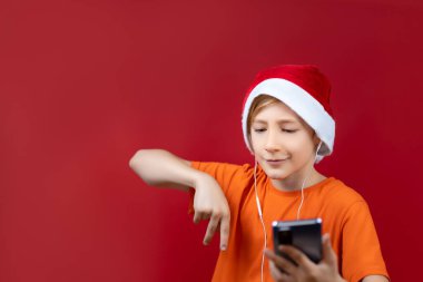 Noel Baba şapkalı bir çocuk önünde bir telefon tutuyor ve Noel motiflerini dinliyor.