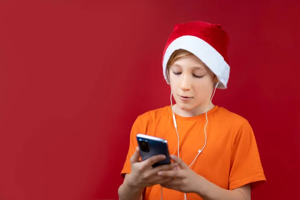 Ein Junge Orangefarbenem Shirt Und Roter Weihnachtsmütze Hält Ein Handy — Stockfoto