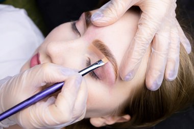 Kaşları kapladıktan sonra işi bitirmiş. Beyaz eldivenli bir usta makyaj fırçalı bir ton kremi sürmüş.