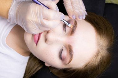 Modelin yüzünü yakın plan çekimde, usta kat işleminden sonra kaşının altına bir ton kremi sürer.