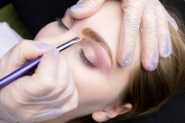 the eyebrow lamination master holds the model\'s eyebrow and applies a toning cream to redness