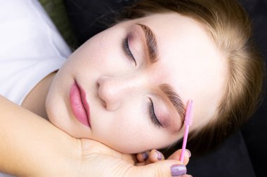 Kaş kaplama işleminden sonra güzel bir sarışın mankenin yüzü, usta bir fırçayla kaşları tarar.