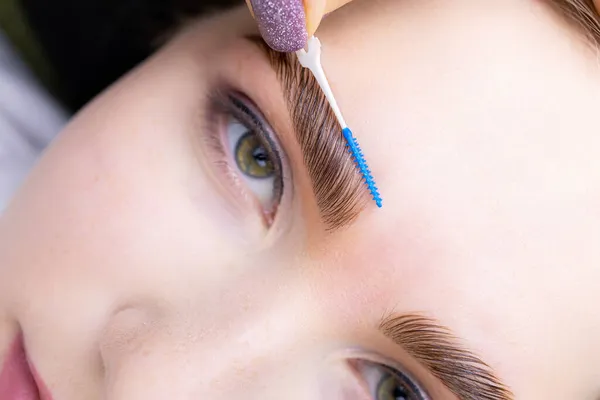 lamination of eyebrows with the help of the composition, the master combs the eyebrow hairs at an angle of forty-five degrees