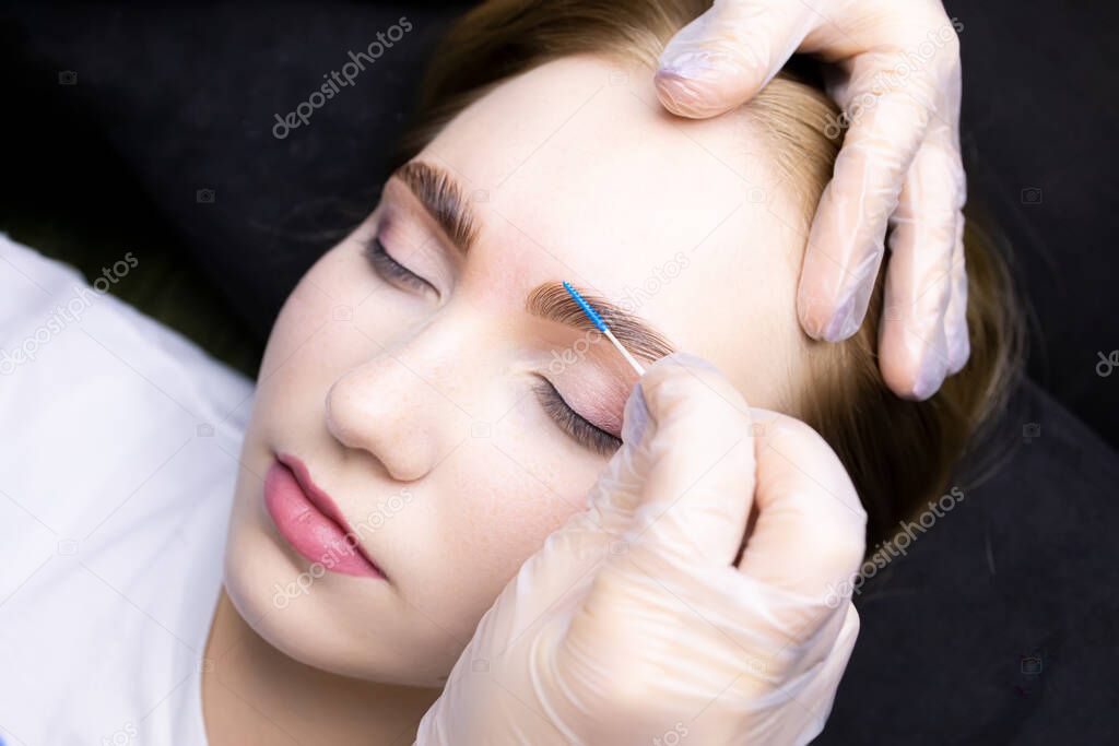 the model after the procedure of lamination of eyebrows with the help of compositions, the master puts the hairs in the eyebrows with the help of blue brushes