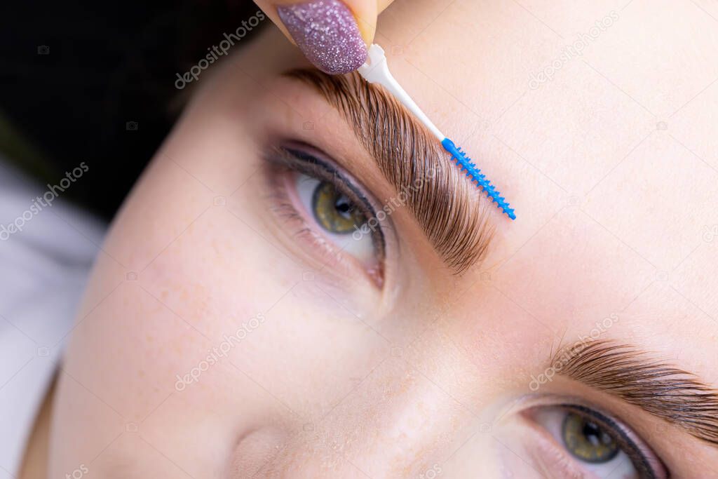 lamination of eyebrows with the help of the composition, the master combs the eyebrow hairs at an angle of forty-five degrees