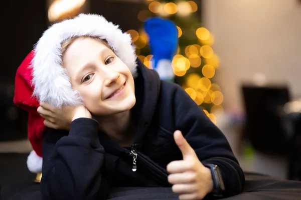 Счастливый Мальчик Рождественской Шляпе Санта Катается Руках Улыбается Фоне Рождественской — стоковое фото