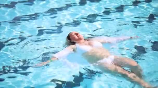 Schöne Frau in Weiß entspannt sich beim Schwimmen auf dem Rücken im Pool — Stockvideo