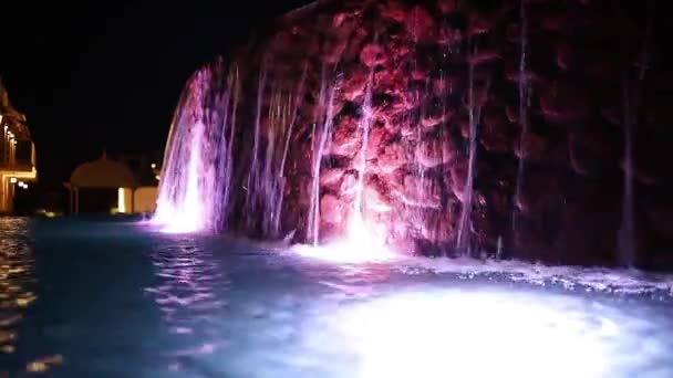 Wodospad wpada nocą do jarzącego się basenu. — Wideo stockowe