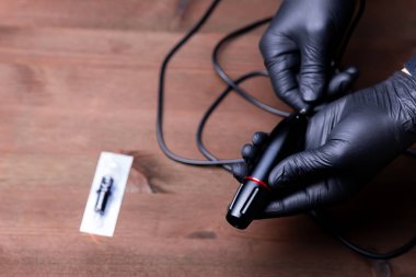 Siyah eldivenli bir makyaj sanatçısının elleri dövme makinesine kablo sokmaya çalışıyor.