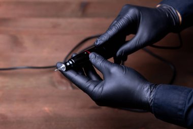 Siyah tıbbi eldivenli daimi makyaj uzmanının elleri dövme makinesindeki tek kullanımlık kartuşun içine konur.