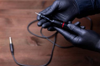 Siyah tıbbi eldivenli, tek kullanımlık dövmeli bir kartuşu dövme makinesine sokmaya çalışan bir makyaj sanatçısının elleri.