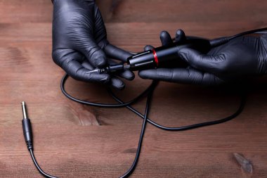 Siyah tıbbi eldivenli, tek kullanımlık dövmeli bir kartuşu dövme makinesine sokmaya çalışan bir makyaj sanatçısının elleri.