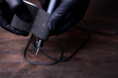 Siyah steril eldivenli bir makyajcının elleri dövme makinesini korumak için elinde bir bant tutuyor.