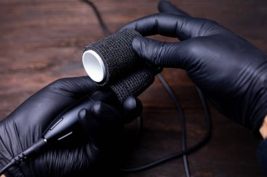 Siyah steril eldivenli bir makyajcının elleri dövme makinesini korumak için elinde bir bant tutuyor.