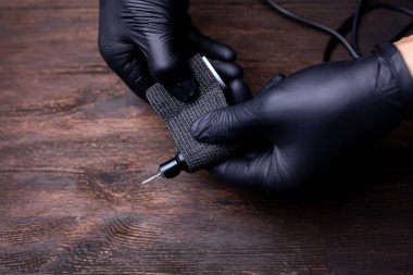 Siyah steril eldivenli bir makyaj sanatçısının elleri siyah bir bandaj bandıyla sarılmış dövme makinesini koruyor.