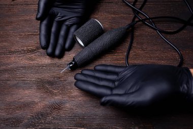 Siyah steril eldivenli bir makyaj sanatçısının elleri siyah bir bandaj bandıyla sarılı bir dövme makinesini işaret ediyor.