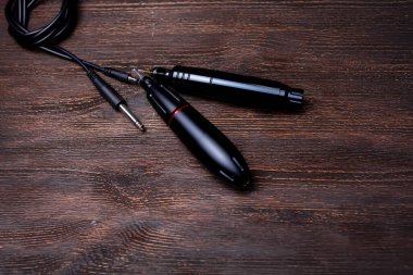 Güç kablosu olan iki siyah dövme makinesi ahşap bir masada yatıyor.