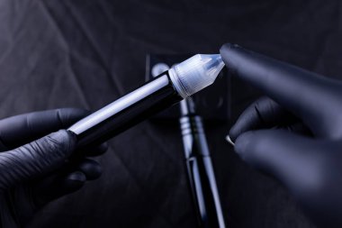 Siyah eldivenli üstadın elleri kalıcı kaş makyajı için pigment şişesi tutuyor.