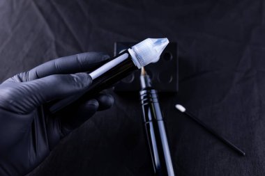 Siyah eldivenli üstadın elleri kalıcı kaş makyajı için pigment şişesi tutuyor.